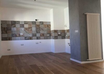 Ristrutturazione cucina con parete paraschizzi in piastrelle con motivi geometrici, pilastro grigio con termoarredo e parquet